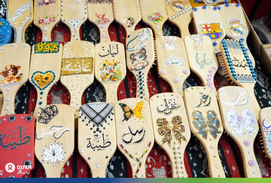 نظرة مقربة على فرشاة شعر خشبية زينتها آمال يدوياً بأسماء وزخارف مبهجة. كل قطعة تنتجها هي مشروع صغير بحد ذاته، يبرز كيف يمكن للمهارة المهنية والفنية للمرأة أن تتحول إلى منتج اقتصادي ينافس في السوق المحلي.
